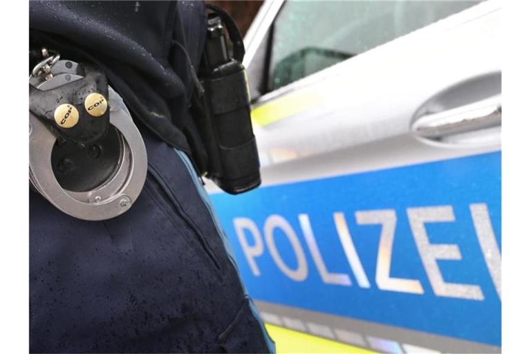 Ein Polizist mit Handschellen und einer Pistole am Gürtel steht vor einem Streifenwagen. Foto: Karl-Josef Hildenbrand/dpa