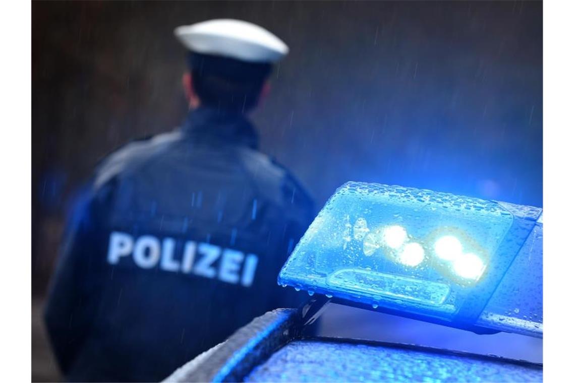 Mann geht mit Machete auf Polizisten los: Angeschossen Ein Polizist steht im Regen vor einem Streifenwagen dessen Blaulicht aktiviert ist. Foto: Karl-Josef Hildenbrand/dpa/Illustration