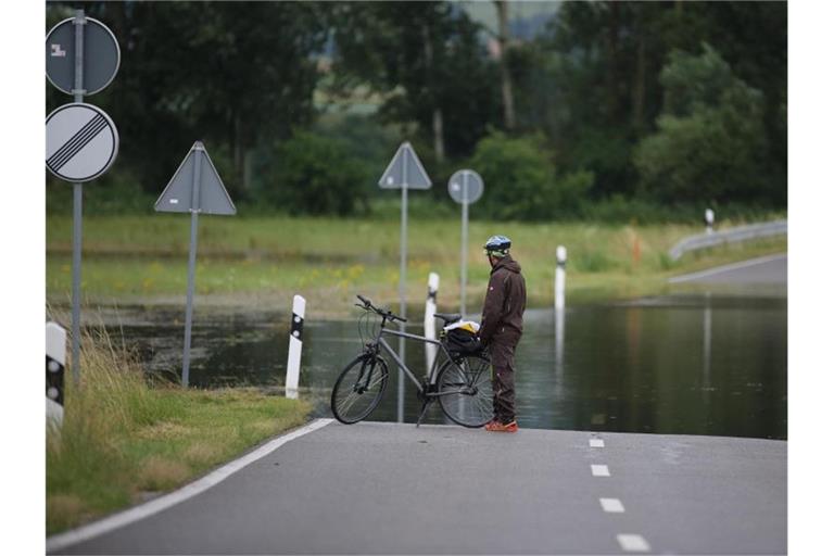 Ein Radfahrer steht an einer überfluteten Straße. Foto: Thomas Warnack/dpa/Symbolbild