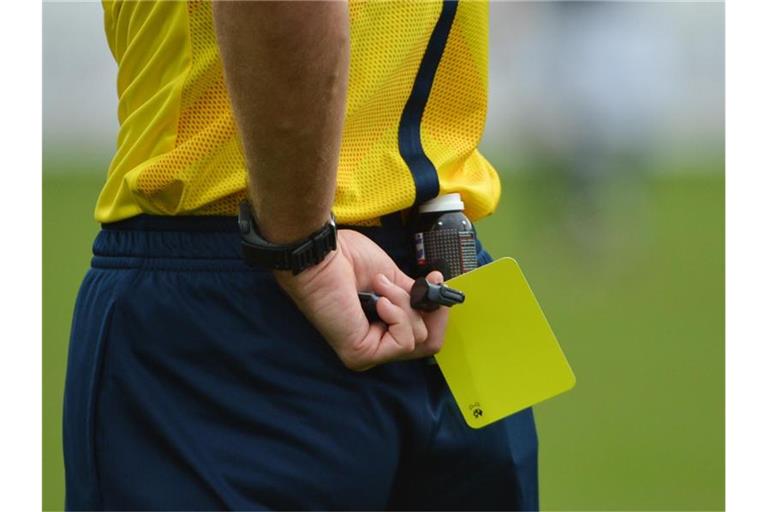 Ein Schiedsrichter hält die Gelbe Karte bereit. Foto: Arne Dedert/dpa/Archivbild