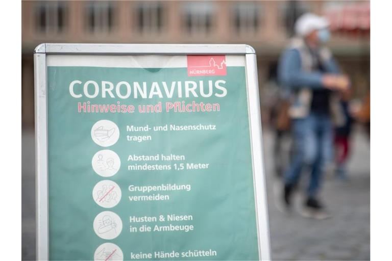 Ein Schild informiert Passanten auf dem Nürnberger Hauptmarkt über die Maskenpflicht und weitere Regeln. Foto: Daniel Karmann/dpa