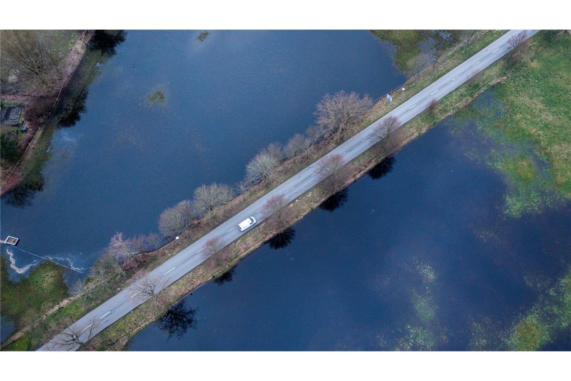 Ein schmaler Grad: Ein Auto fährt auf einer Straße in Mecklenburg-Vorpommern, die zwischen zwei nach starken Regenfällen überfluteten Wiesen liegt.