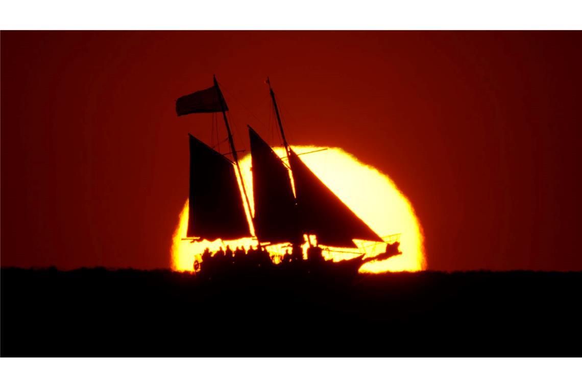 Ein Segelboot zeichnet sich gegen die untergehende Sonne ab, während es im Golf vor der Küste von Treasure Island in Florida segelt.