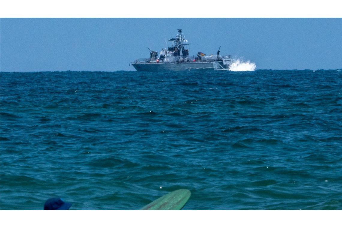 Ein Surfer wartet auf eine Welle, während ein israelisches Marineschiff im Mittelmeer vor der Küste von Hadera patrouilliert.