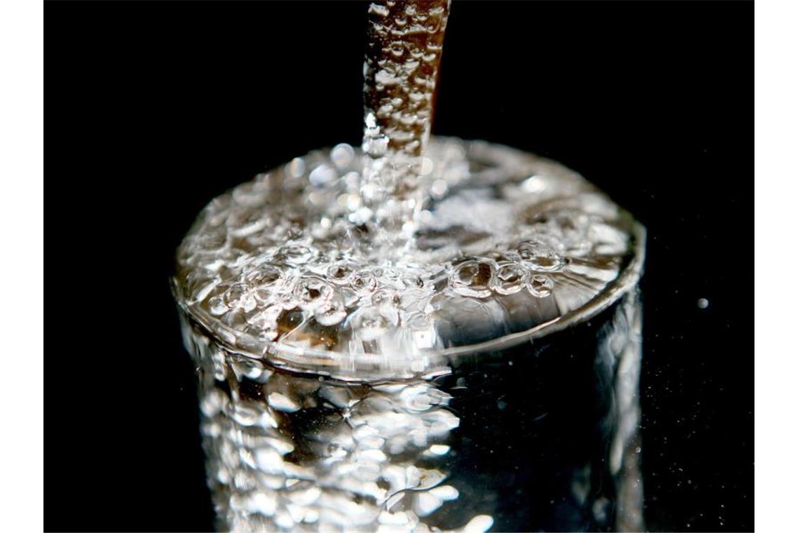 Ein überlaufendes Glas, in das Trinkwasser läuft. Foto: Oliver Berg/dpa/Illustration