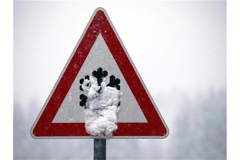 Ein Verkehrsschild, auf dem vor Schnee- und Eisglätte gewarnt wird, ist mit Schnee bedeckt. Foto: Karl-Josef Hildenbrand/dpa/Symbolbild