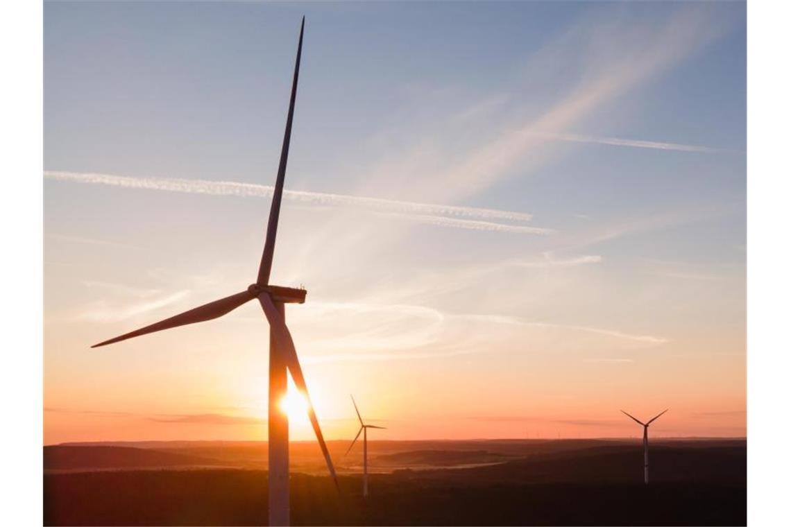 Ein Windrad eines Windparks steht während des Sonnenaufgangs in einem Wald. Foto: Tom Weller/dpa/Archivbild