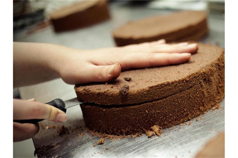 Eine angehende Konditorin schneidet einen Kuchenboden durch. Foto: picture alliance/dpa/Symbolbild