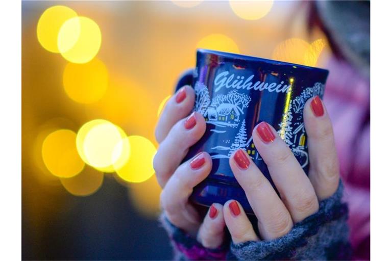 Eine Frau hält eine Tasse mit Glühwein in den Händen. Foto: Jens Kalaene/zb/dpa/Archivbild