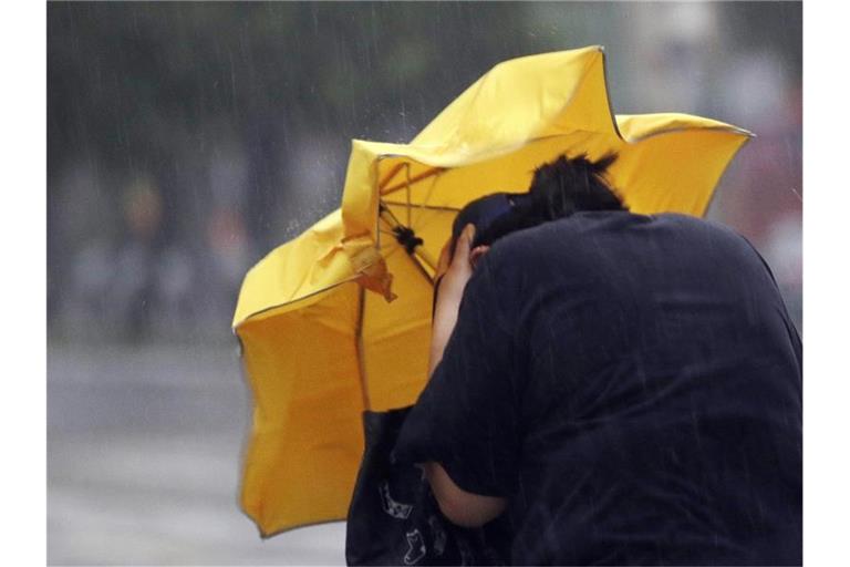 Eine Frau kämpft mit einem Regenschirm gegen Windböen. Foto: Chiang Ying-Ying/AP/dpa/Archivbild