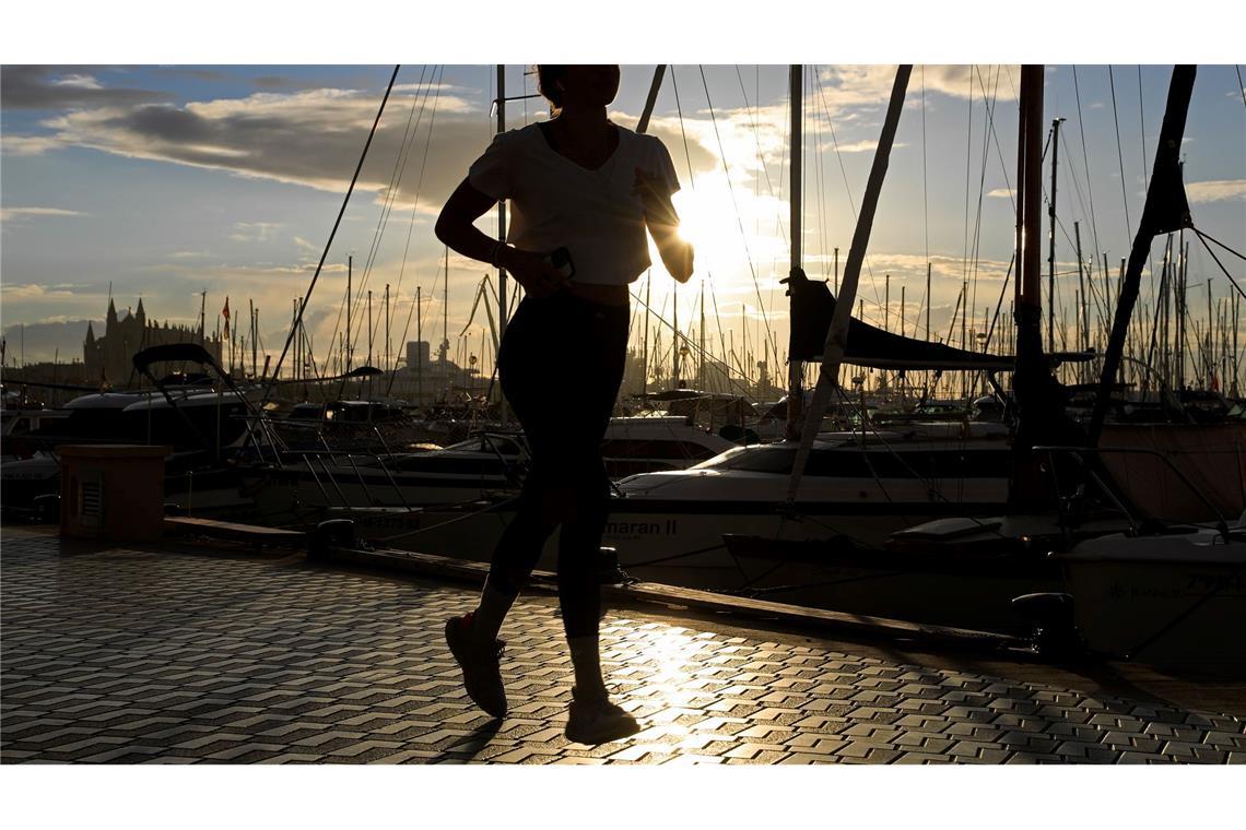 Eine Frau läuft während des Sonnenaufgangs an der Hafenpromenade von Palma auf Mallorca.