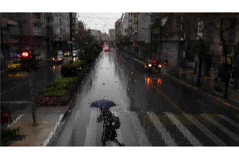 Eine Frau mit Regenschirm überquert eine Straße in Athen.