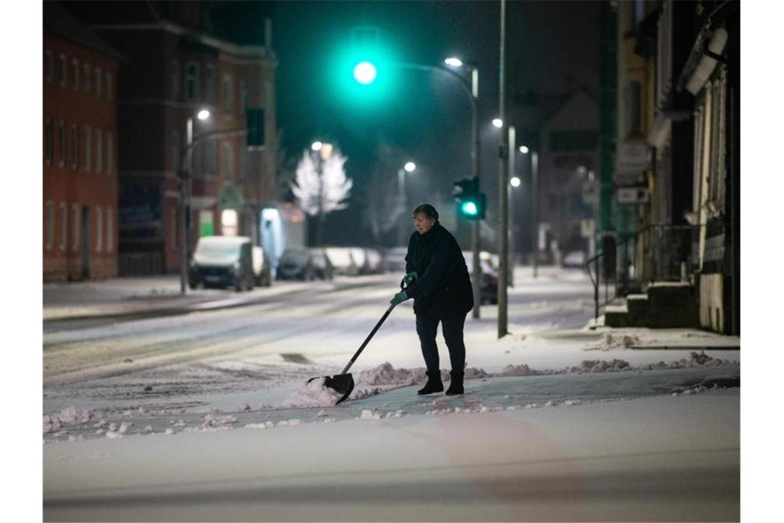 Schneesturm fegt über Deutschland - Meterhohe Verwehungen Eine Frau schippt am frühen Morgen Schnee auf einem Bürgersteig in Gevelsberg. Foto: Jonas Güttler/dpa