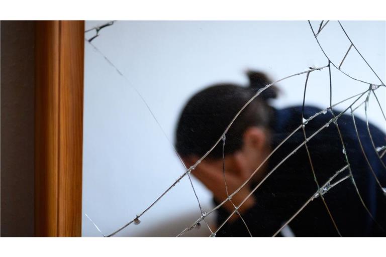 Eine Frau sitzt neben einem gesprungenen Spiegel auf einem Bett und hält ihren Kopf in den Händen. Ein Gesetzentwurf soll Frauen besser vor Gewalt schützen (Symbolfoto).