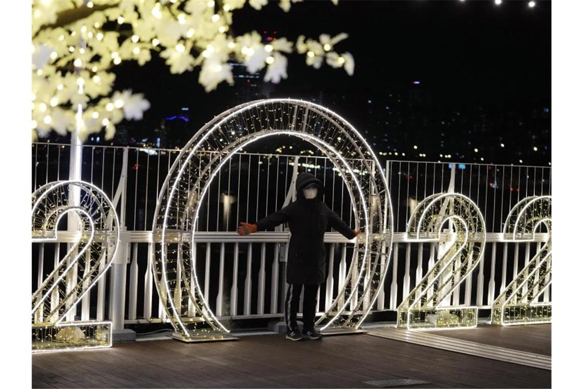 Das neue Jahr startet erneut eher ruhig - Milde Temperaturen Eine Frau steht in Seoul (Südkorea) mit Mund-Nasen-Schutz vor einer beleuchteten Dekoration. Foto: Lee Jin-Man/AP/dpa