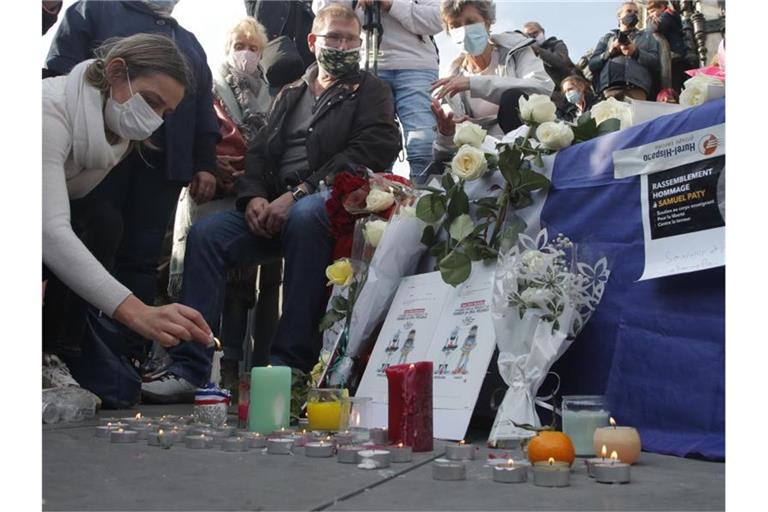 Eine Frau zündet eine Kerze an: Zahlreiche Menschen haben sich nach der brutalen Ermordung eines Lehrers am Wochenende zu einer Solidaritätsdemonstration in Paris versammelt. Foto: Michel Euler/AP/dpa