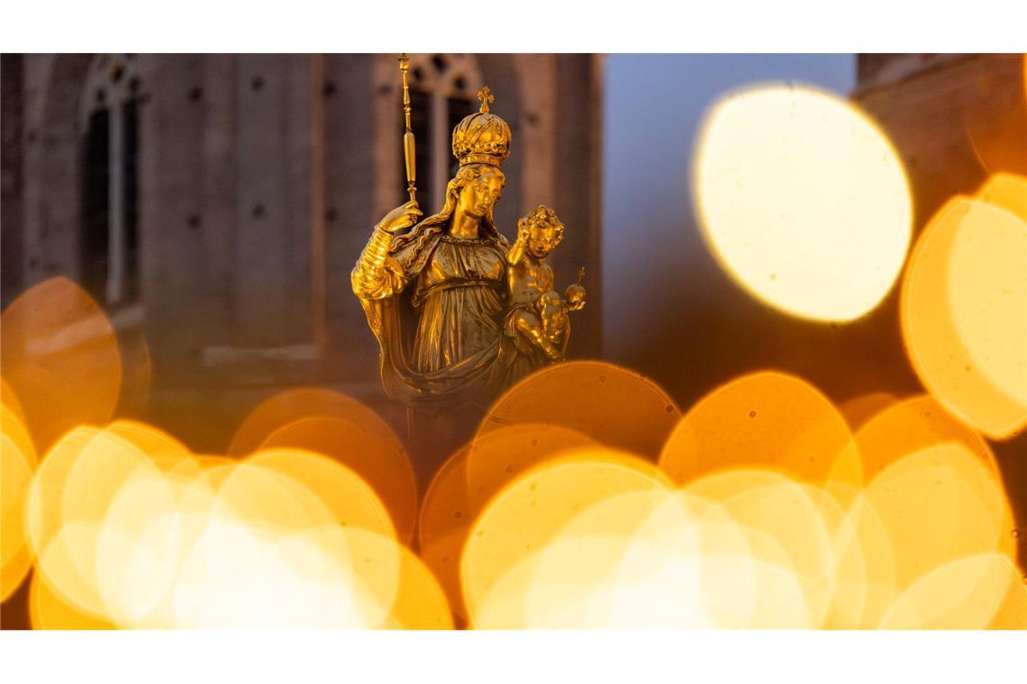 Eine goldene Marienfigur steht auf dem Marienplatz in München im Licht des umliegenden Weihnachtsmarkts.