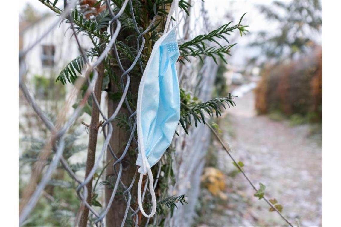 Eine hängen gelassene Maske ist an einem Zaun an einem Gehweg zu sehen. Foto: Bernd Weißbrod/dpa/Archivbild