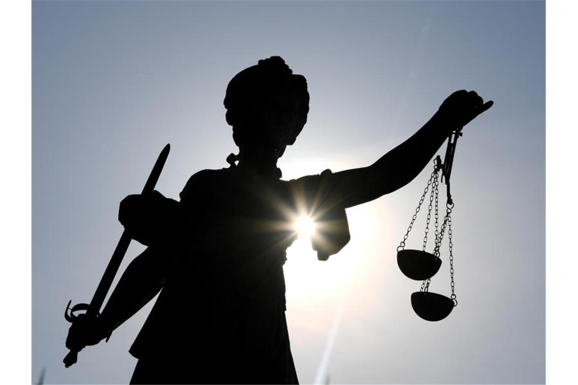 Duo wegen Drohschreiben und Brandanschlag angeklagt Eine Justitia-Statue ist im Gegenlicht zu sehen. Foto: Arne Dedert/dpa/Archivbild