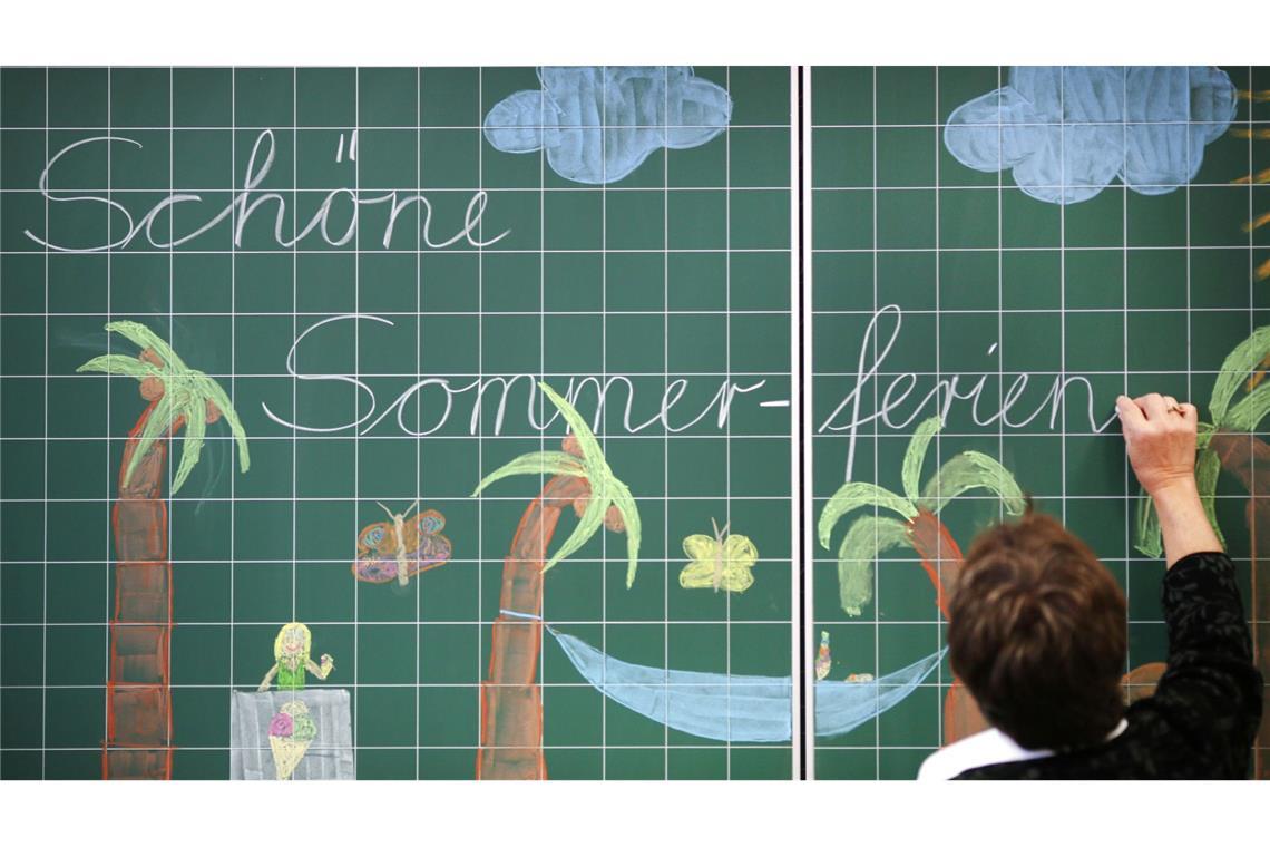 Eine Lehrerin schreibt "Schöne Sommerferien" an die Tafel einer Grundschulklasse. (Archivfoto)