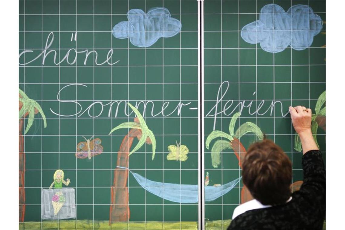 Kretschmann-Vorstoß für kürzere Sommerferien löst Kritik aus Eine Lehrerin schreibt „Schöne Sommerferien“ an eine Tafel. Foto: picture alliance/Ina Fassbender/dpa/Archiv/Illustration