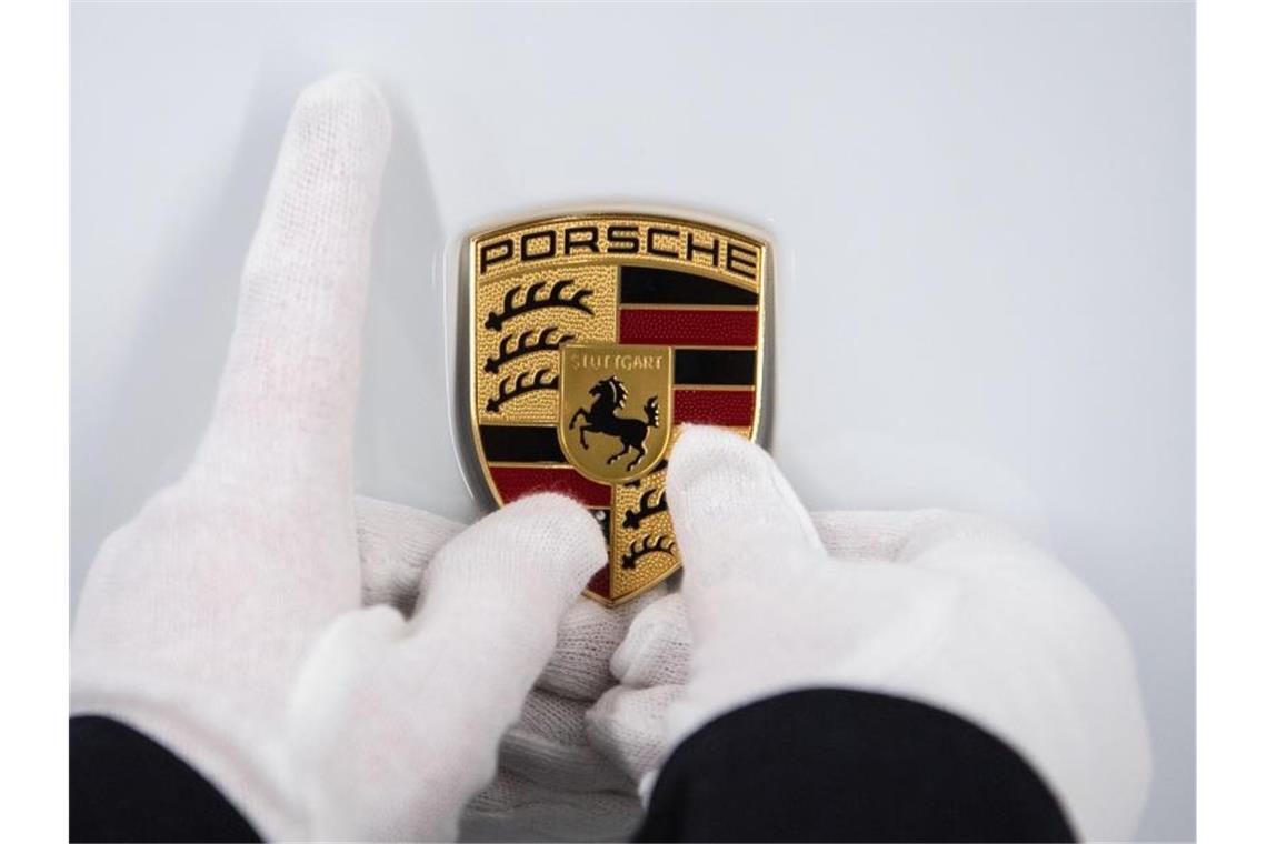 Eine Mitarbeiterin hält ein Porsche-Emblem auf eine Motorhaube. Foto: Marijan Murat/dpa/Symbolbild