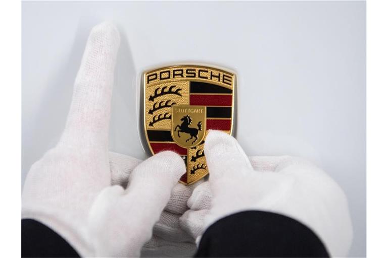 Eine Mitarbeiterin hält ein Porsche-Emblem auf eine Motorhaube. Foto: Marijan Murat/dpa/Symbolbild