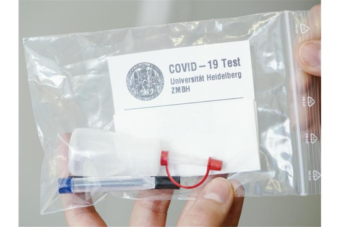 Uni Heidelberg bietet Gurgeltests für Studierende an Eine Mitarbeiterin hält ein Testkit des Gurgeltests in den Händen. Foto: Uwe Anspach/dpa