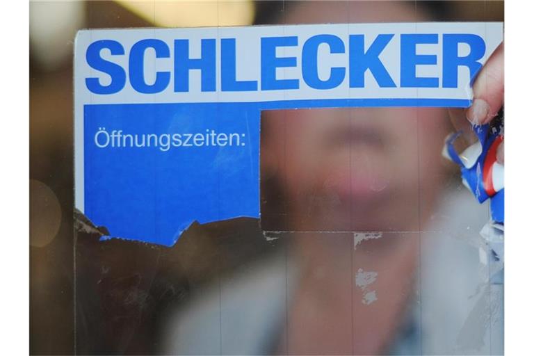 Eine Mitarbeiterin von Schlecker reißt das Firmenlogo von der Eingangstür. Foto: picture alliance / Julian Stratenschulte/dpa/Symbolbild