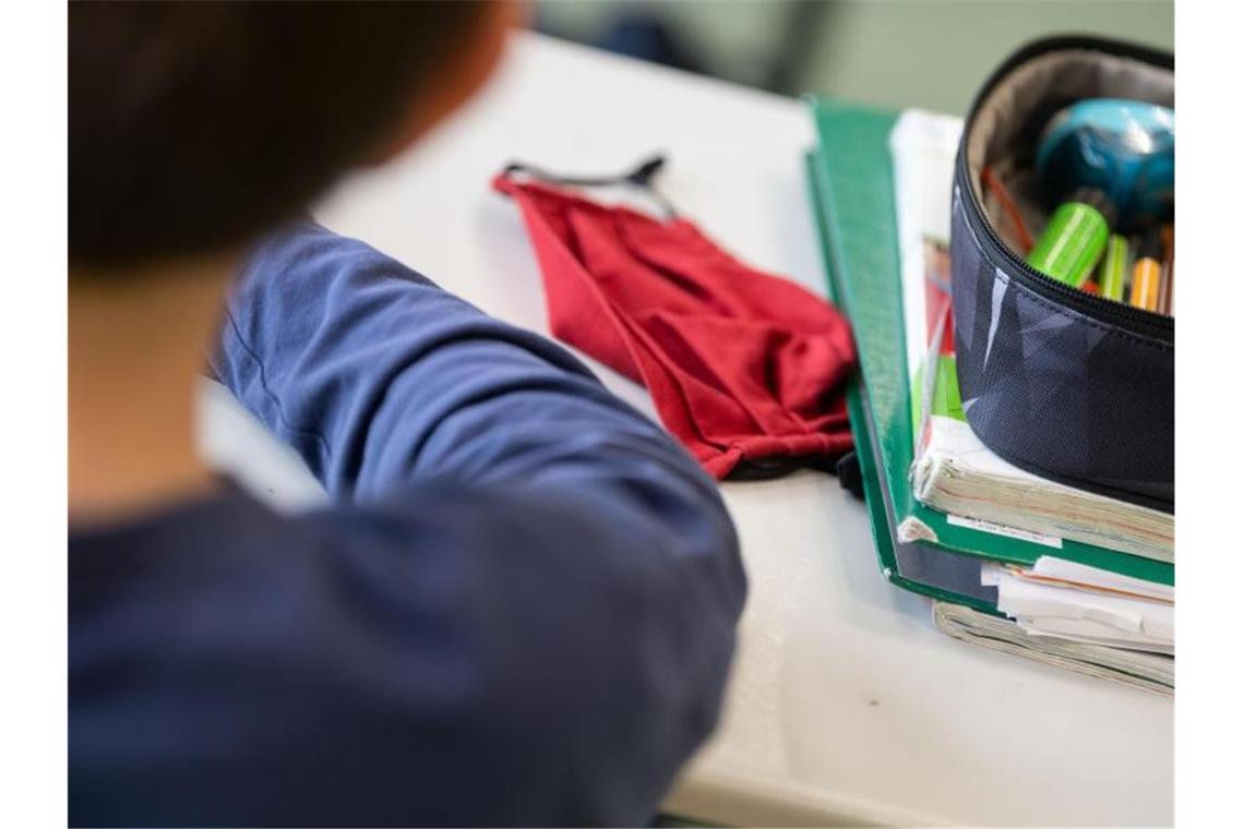 Eine Mund-Nasen-Bedeckung liegt während einer Unterrichtsstunde auf einem Schultisch. Foto: Marijan Murat/dpa/Archivbild