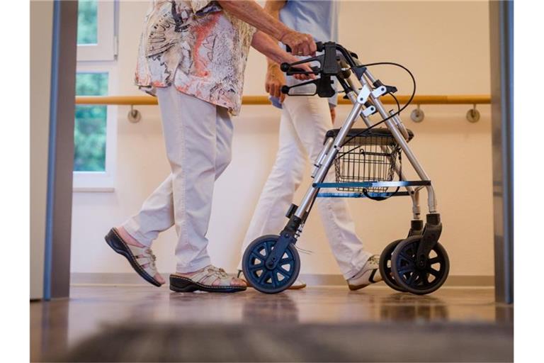 Eine Pflegekraft geht in einem Pflegeheim mit einer älteren Frau über einen Korridor. Foto: Christoph Schmidt/dpa/Archiv