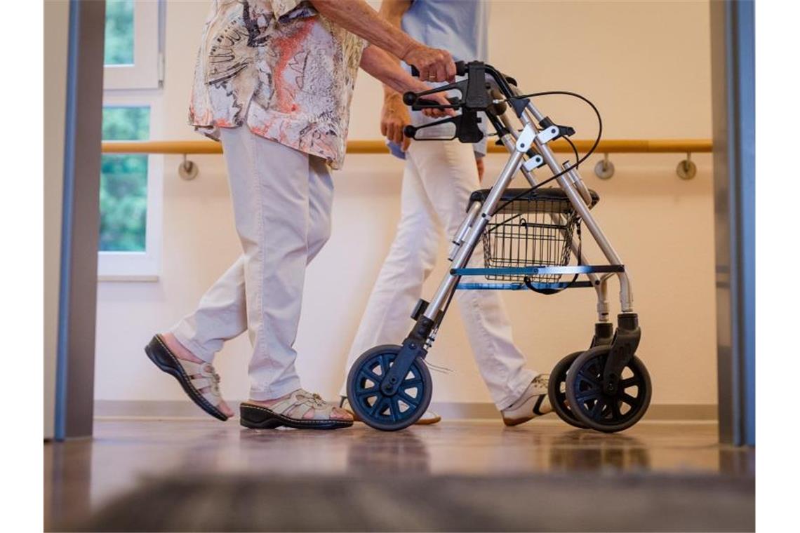 Eine Pflegekraft geht in einem Pflegeheim mit einer älteren Dame über einen Korridor. Foto: Christoph Schmidt/dpa/Symbolbild