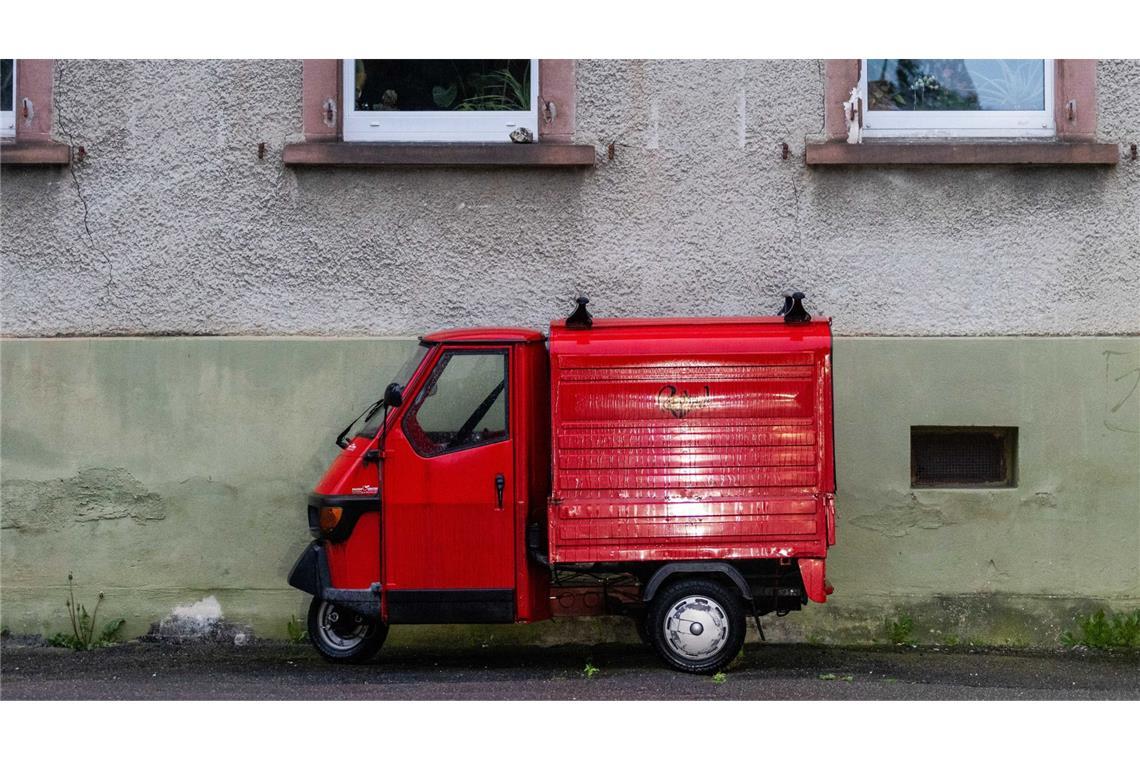 Eine rote Piaggio „Ape“ steht vor einem Haus.