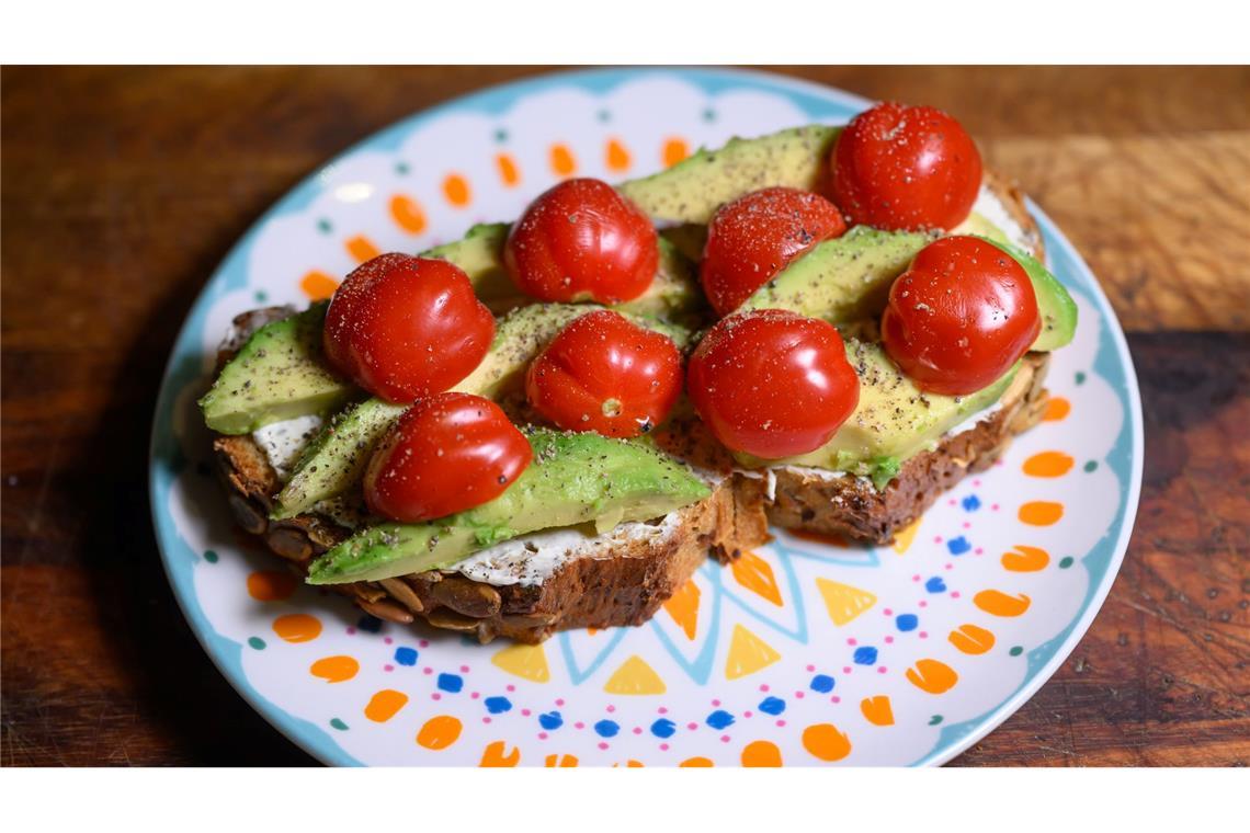 Eine Scheibe Kürbiskernbrot mit Avocado und Tomaten. Viele jüngere Leute in Deutschland sehen sich eher als Avocadobrot- denn Wurstbrot-Typ. (Symbolbild)