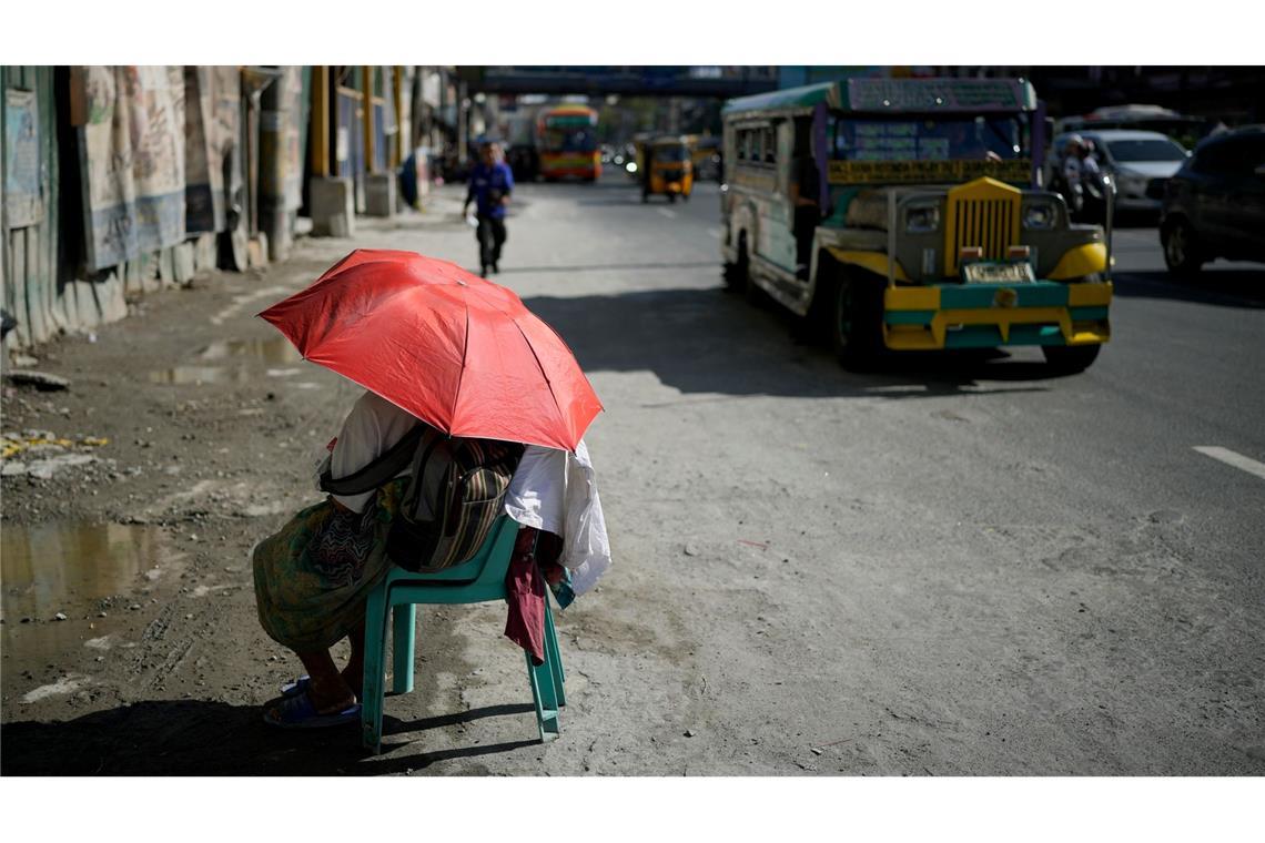 Eine Straßenverkäuferin schützt sich in Manila mit einem Regenschirm vor der Sonne.