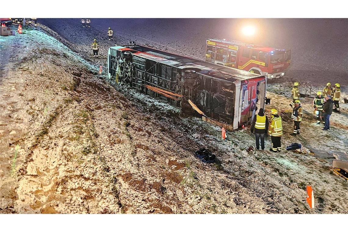 Einsatzkräfte der Feuerwehr stehen neben einem umgekippten Linienbus an der Unfallstelle im Landkreis Ludwigsburg.