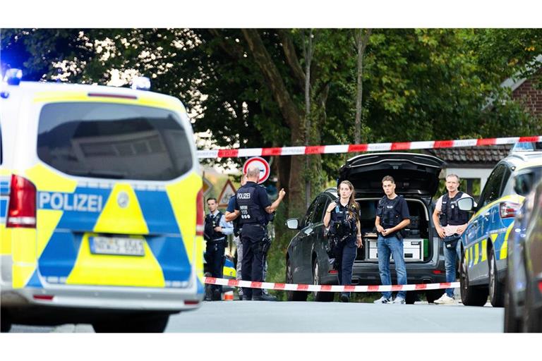 Einsatzkräfte der Polizei stehen am Tatort zwischen Fahrzeugen.