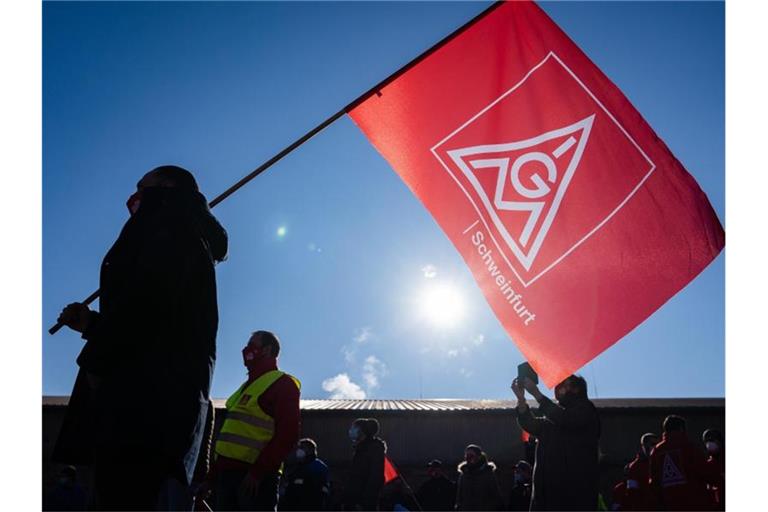 Ein Teilnehmer eines Warnstreicks schwenkt eine Fahne mit dem Logo der IG Metall. Foto: Nicolas Armer/dpa/Symbolbild