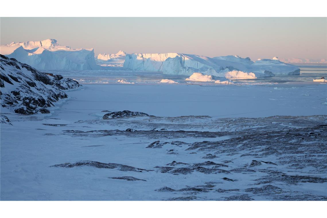 Eisberge ragen im Ilulissat-Eisfjord hinter einer verschneiten Gesteinslandschaft in die Höhe.