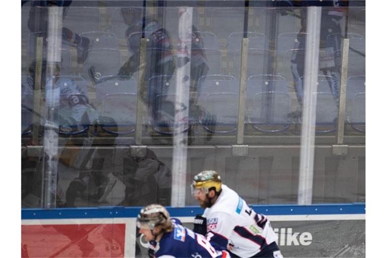 Eishockeyspieler spiegeln sich vor leeren Rängen in der Bande. Foto: Bernd Thissen/dpa/Symbolbild