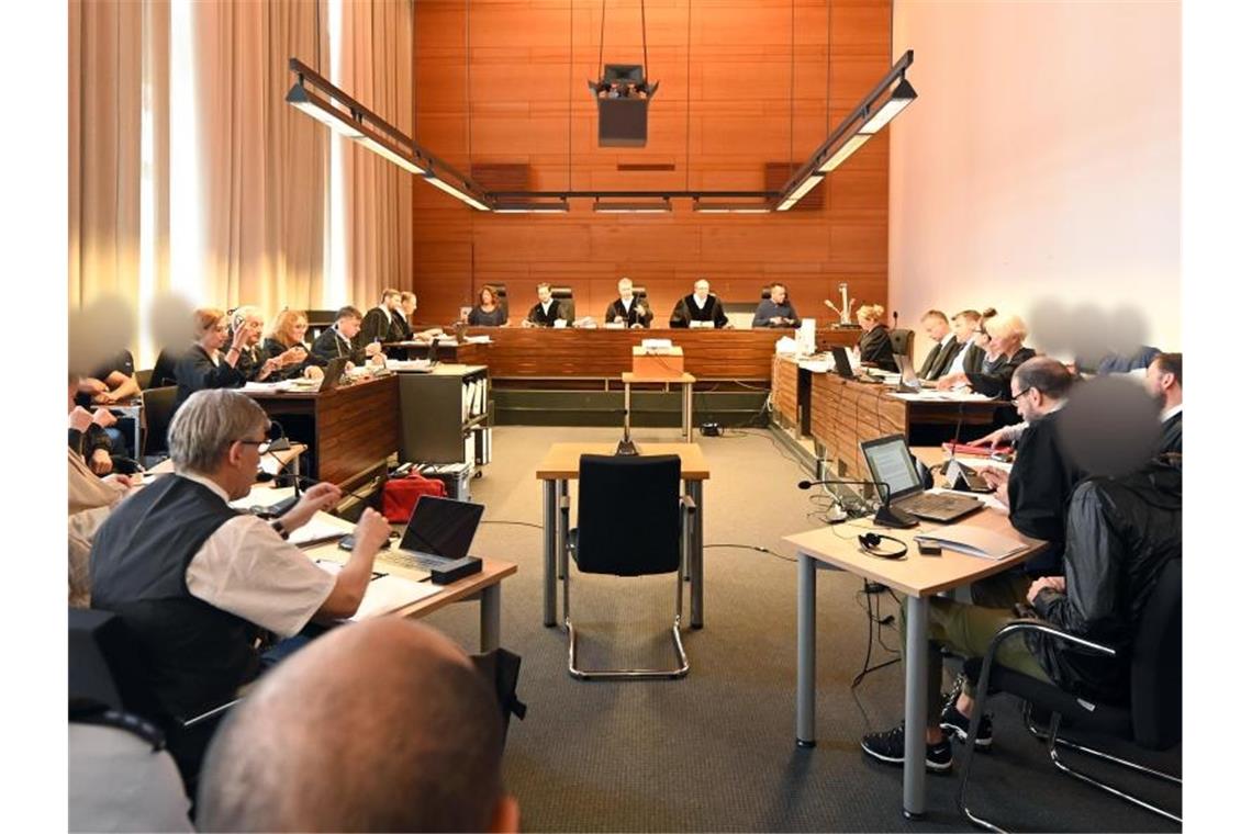 Elf Angeklagte und Justizbeamte sitzen im Landgericht seitlich hinter den Anwälten. Foto: Patrick Seeger/dpa/Archivbild
