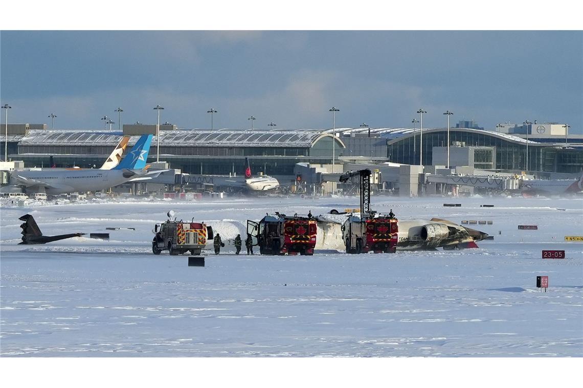 Feuerwehrleute des Toronto Pearson International Airport arbeiten an einem auf dem Rücken liegenden Flugzeug der Delta Air Lines.