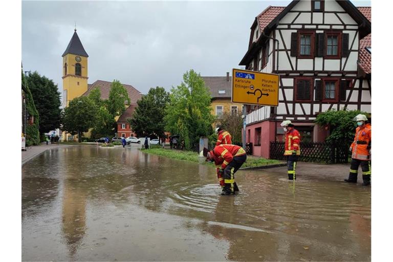 Feuerwehrleute stehen nach einem Unwetter auf einer überfluteten Straße. Foto: Thomas Riedel/dpa