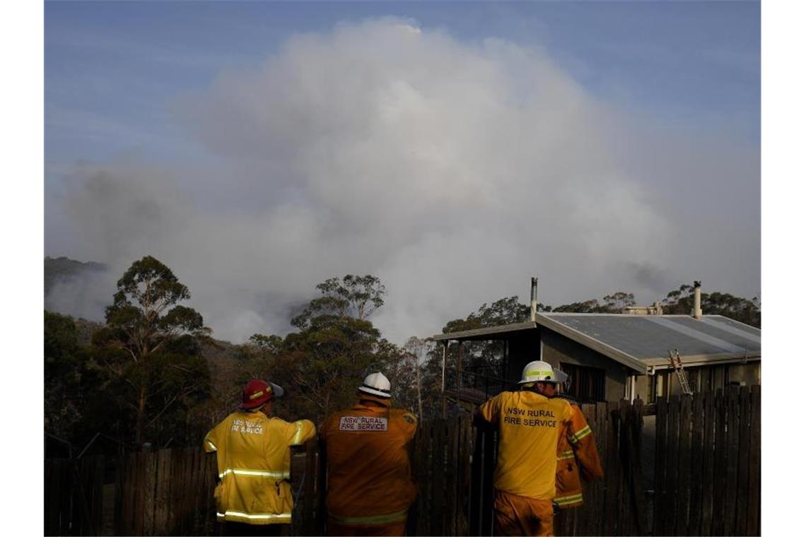 „Megafeuer“ in Australien - und die Zahl der Toten steigt Feuerwehrmänner beobachten aufsteigende Rauchwolken eines Buschfeuers bei Penrose südlich von Sydney. Foto: Dan Himbrechts/AAP/dpa