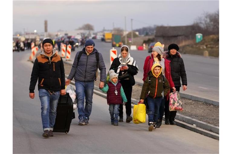 Flüchtlinge, die vor dem Konflikt in der Ukraine fliehen, gehen mit ihrem Gepäck eine Straße entlang. Foto: Petr David Josek/AP/dpa/Archivbild