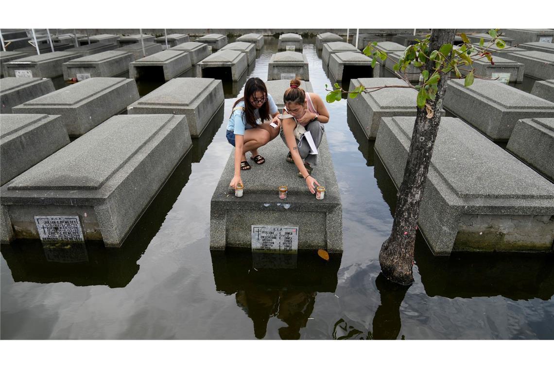 Frauen stellen nach Tropensturm Trami auf einem überschwemmten Friedhof auf den Philippinen Kerzen auf.