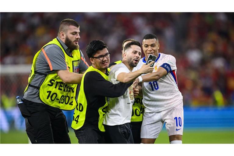 Für ein Selfie mit Frankreichs Kylian Mbappé (r.) ist ein Flitzer auf das Spielfeld gelaufen. Er wird von Ordern aufgehalten.