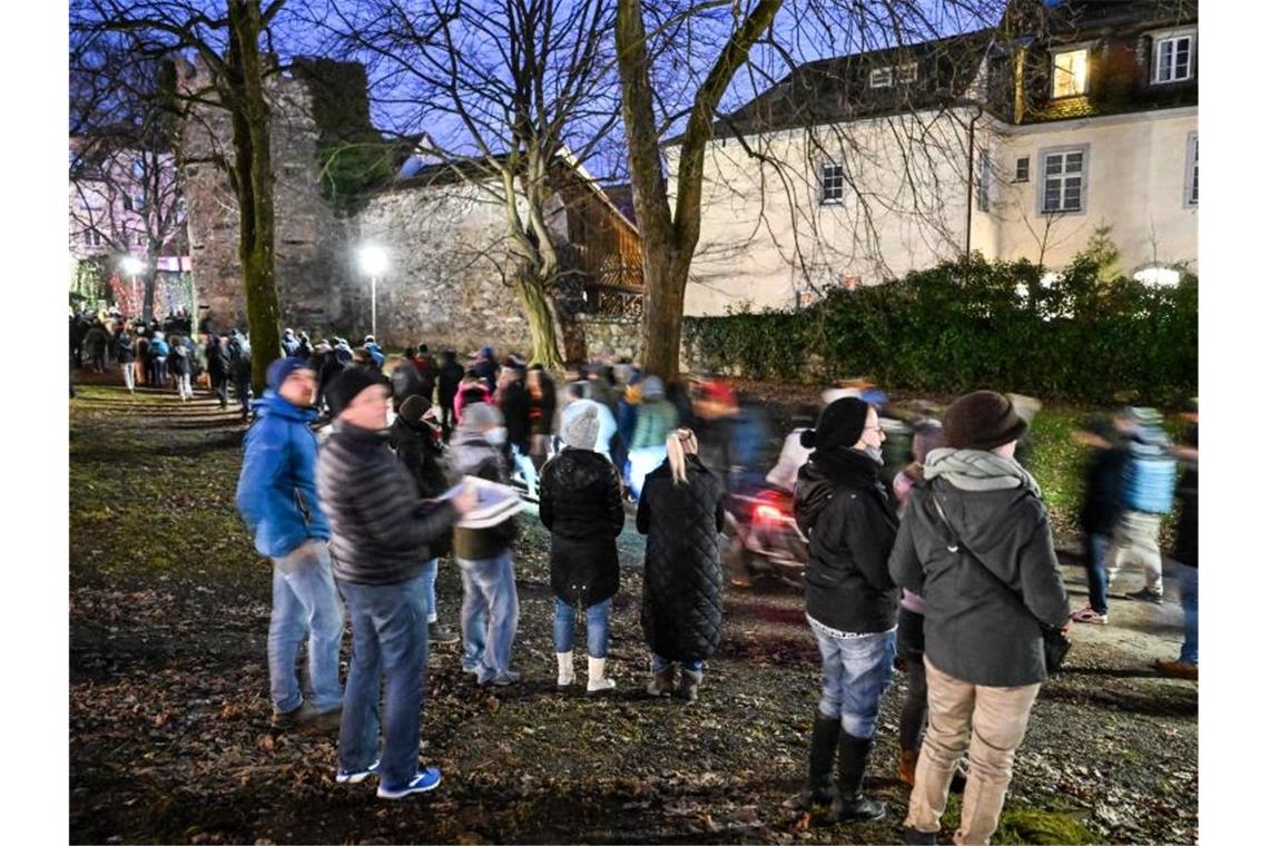 Gegner der Coronapolitik gehen durch die Innenstadt von Ravensburg, während mehrere Passanten sich den Demonstrationszug anschauen und einer nebenbei Pizza isst. Foto: Felix Kästle/dpa