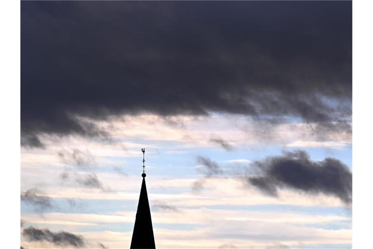 Hinter dem Turm der Pfarrkirche St.Cornelius ziehen Wolken. Foto: Federico Gambarini/dpa/Symbolbild