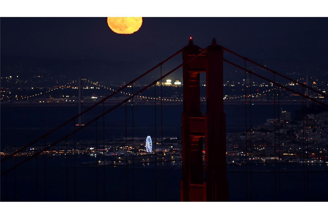 Hinter der Golden Gate Bridge ist am Himmel ein goldfarbener Vollmond zu sehen